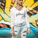 woman in white long sleeve shirt and blue denim shorts standing beside yellow and black wall